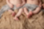 Twin newborn baby feet peak out from beneath a gray wrap while the babies are posed on a tan flokati rug as photographed by Tiffany Edwards, newborn photographer in Billings, Montana