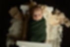 A newborn baby boy wrapped in green stares upward from the tiny bed where he lays, against a boho set up as photographed by Tiffany Edwards Newborn Photographer in Billings Montana in home studio-style session