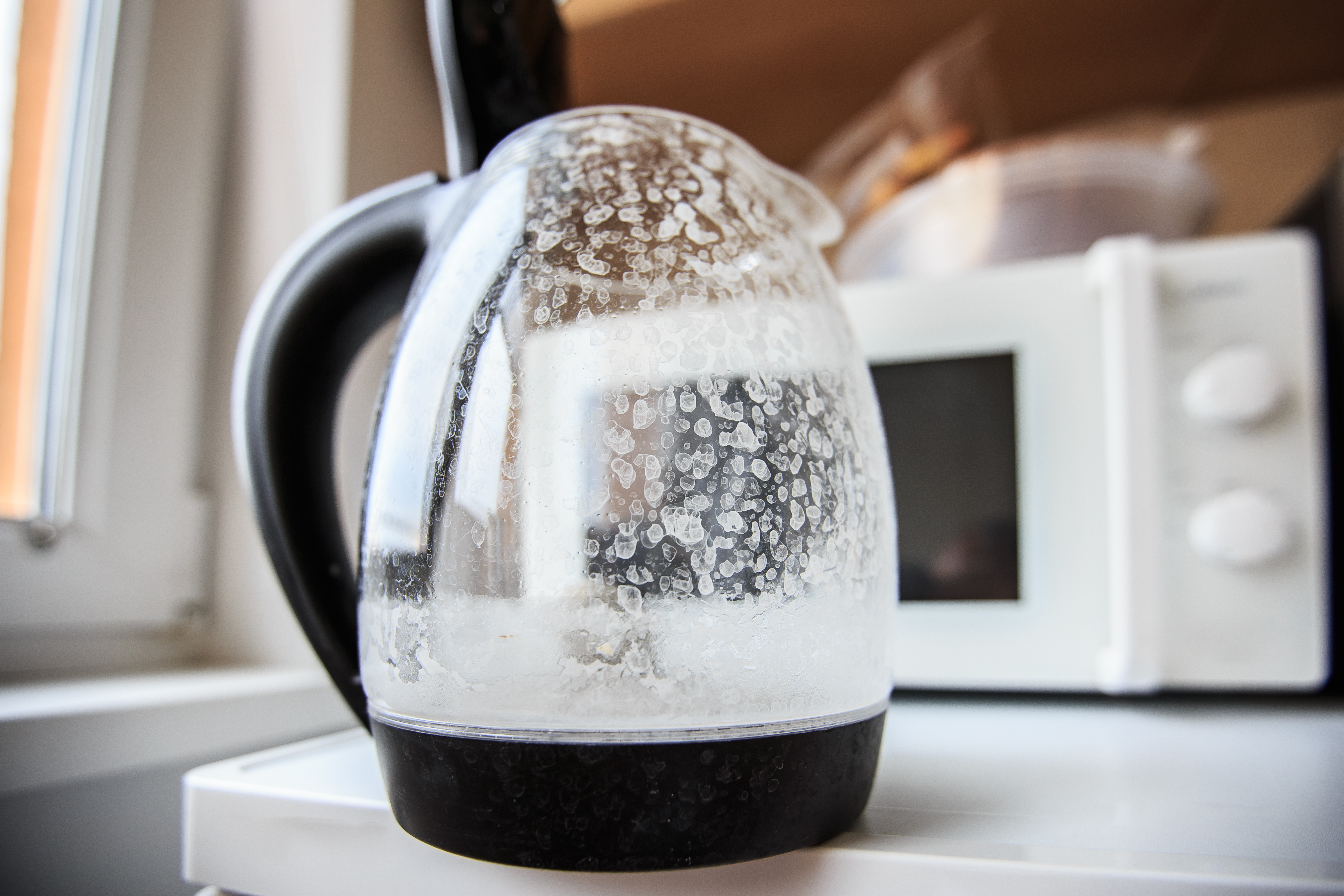 Photograph of a clear coffee pot with cloudy white-ish marks and dots from hard water mineral deposits.
