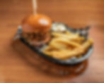 Pulled Pork burger with slaw, fries and aioli, in a basket on a wooden table.. Warm, inviting setting.