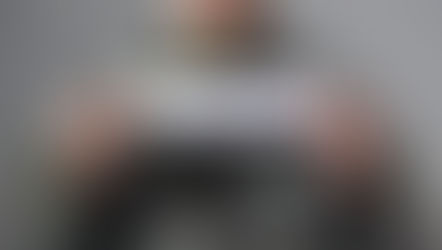 Person in camouflage uniform holding a sign reading "Heal Me" against a gray brick wall, conveying a plea or emotional appeal.