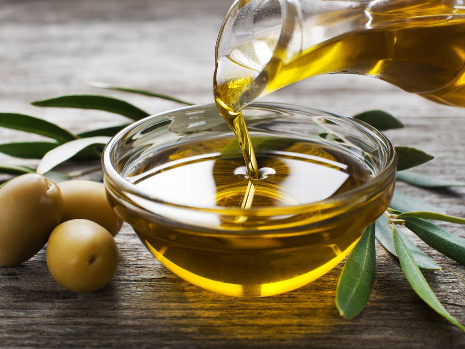 Olive oil pouring into a bow with olives and olive leaves around it