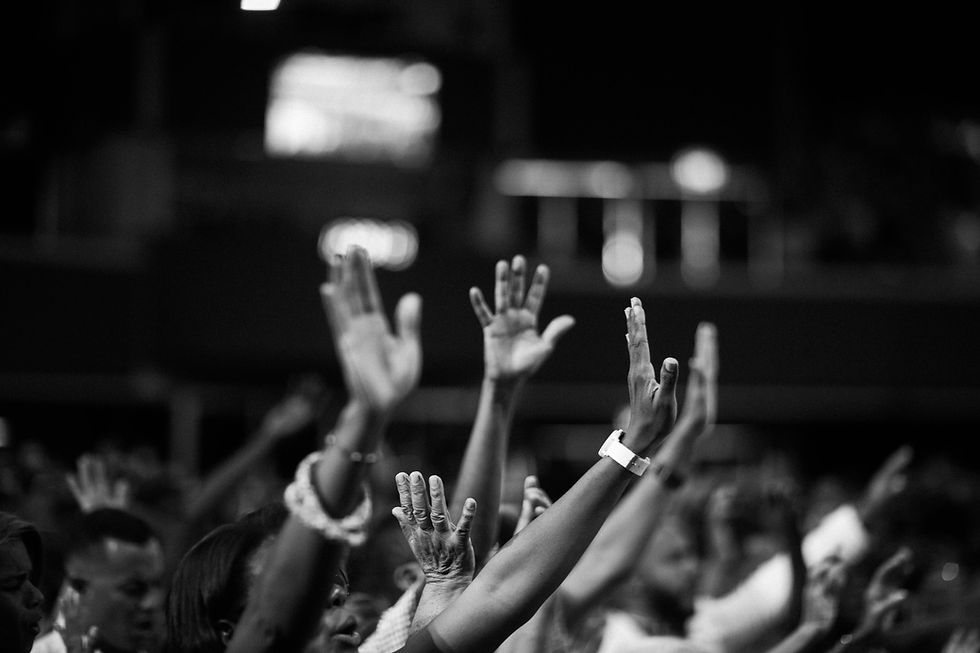 Black and white photo showing a church praise session with various arms being outstretched in the air.