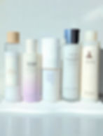 Five skincare toner bottles arranged in a row on a white surface, featuring brands like Haruharu and Laneige. Soft lighting and minimal design.
