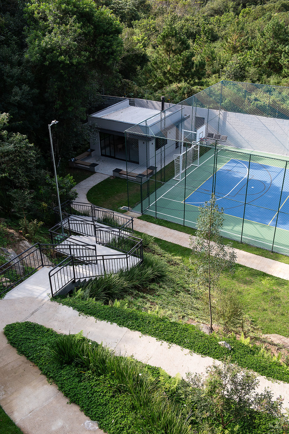 vista de cima da área comum do condomínio sierra vista, com a presença maciça de verde, da quadra poliesportiva e do grill com lounge externo