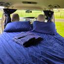 Double bed inside a campervan made up with pillows, folded towels, and neatly arranged bedding.