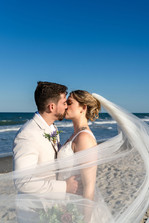 Bride and groom kissing on the beach with veil blowing in wind and ocean in background