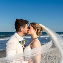Bride and groom kissing, with ocean in the background and veil swopping in front of the camera. Photo taken during wedding at Harbour House in Florida. Photo by Pixel Groves