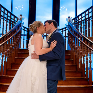 Bride and groom kissing on grand staircase inside elegant venue during wedding day