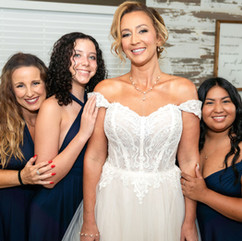 Bride standing in her wedding gown surrounded by bridesmaids smiling before the ceremony
