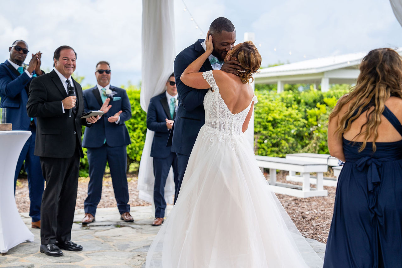 Bride and groom sharing a joyful kiss as wedding party cheers behind them