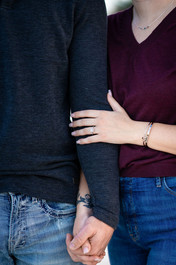 Close-up of an engaged couple standing side by side, holding hands with the woman’s arm wrapped around her partner’s.