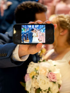 Guest holding smartphone recording bride and groom during wedding ceremony