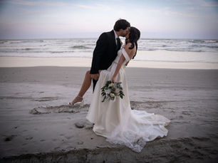Bride and groom kissing on the beach during wedding portrait with ocean waves in the background