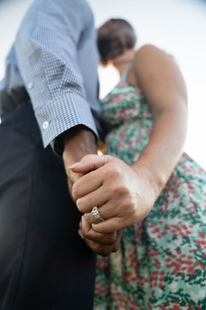 Close-up of a couple holding hands, showing the engagement ring as they lean in for a kiss.