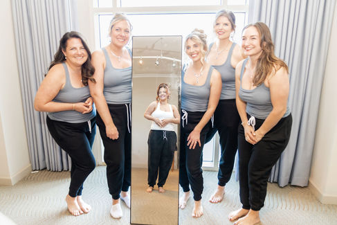 Bride and bridesmaids standing together in front of mirror wearing matching outfits during wedding prep