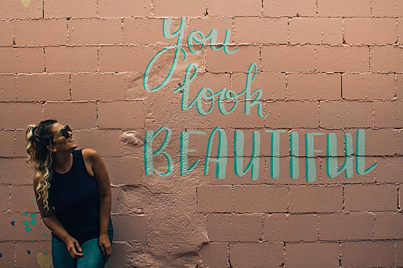femme qui regarde un mur avec l'inscription "you look beautiful"