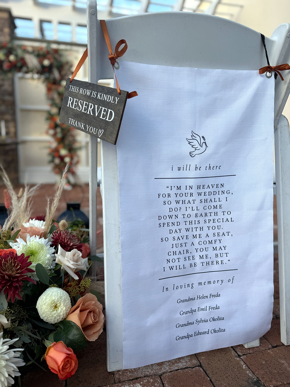 White chair with a reserved sign and memorial cloth, surrounded by flowers, setting a sentimental wedding atmosphere in a decorated venue.