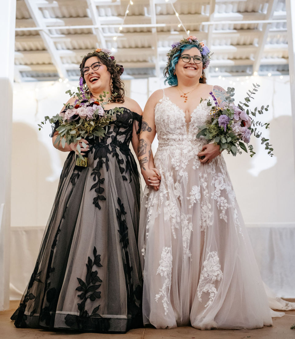 Two queer women smiling and holding hands during their wedding ceremony.