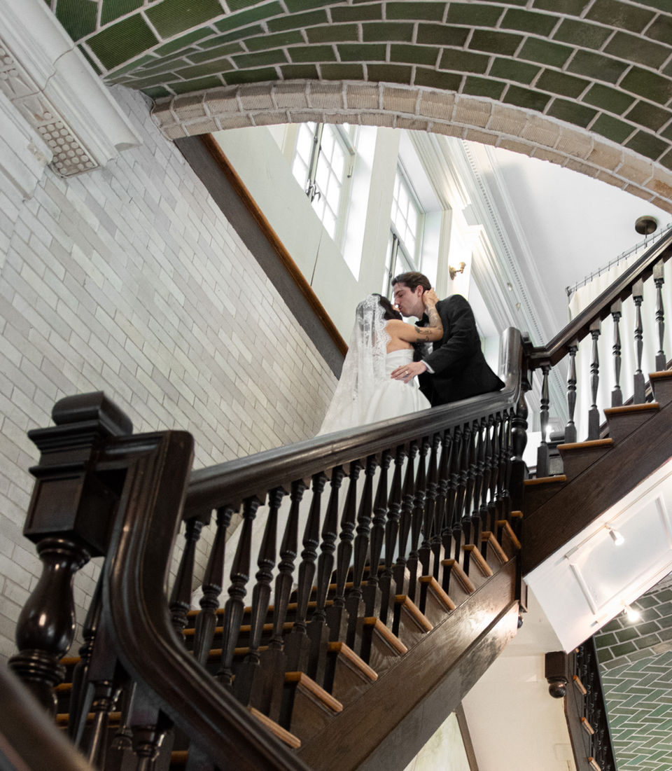 Romantic kiss between a bride and groom on a dramatic ornate staircase.