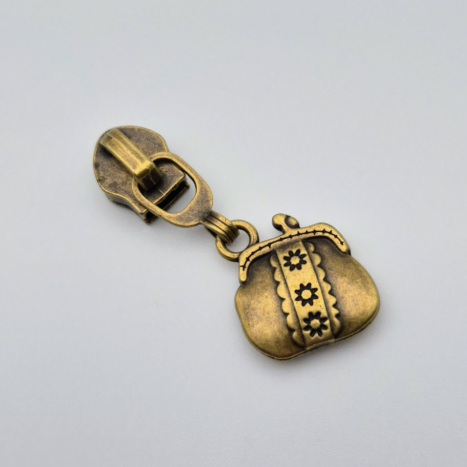 Thumbnail: Close-up of antique brass purse zipper pull with floral detailing, shaped like a coin purse for handmade bags.