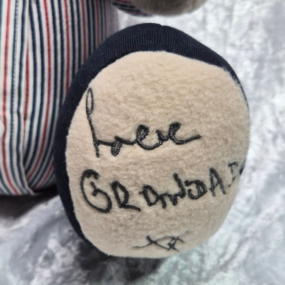 Close‑up of a memory bear paw featuring stitched handwriting that reads “Love Grandad xx,” recreated from an original