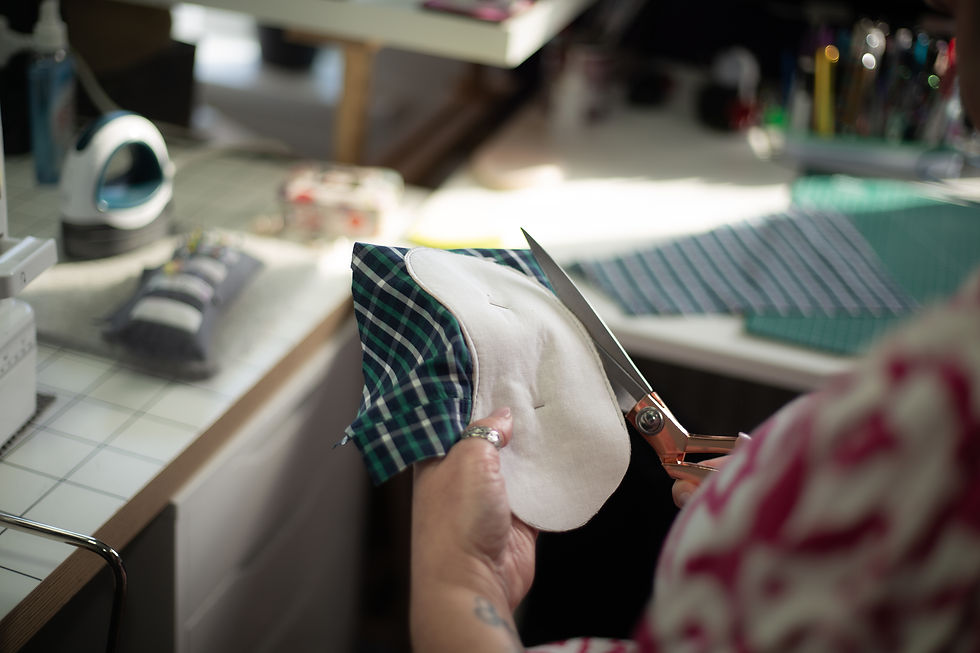 Hands holding a soft grey handmade keepsake with the word am embroidered on it while working in a sewing studio.