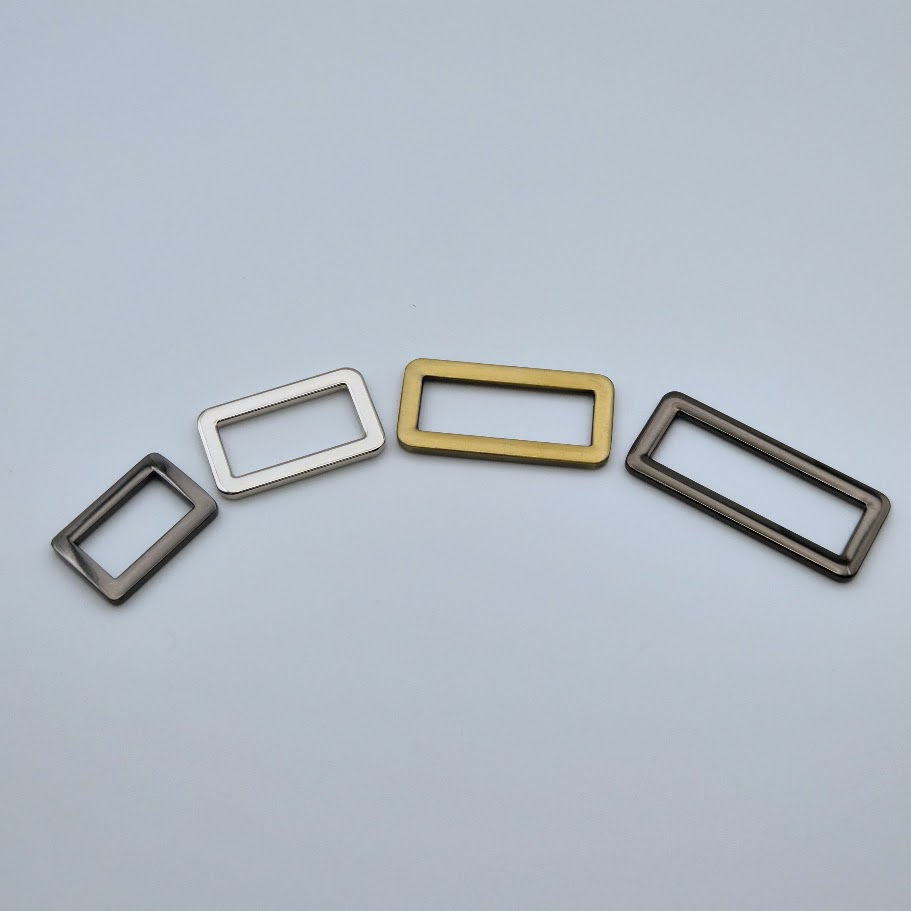 "Four flat rectangular D-rings in gunmetal, silver, brushed brass, and black finishes,