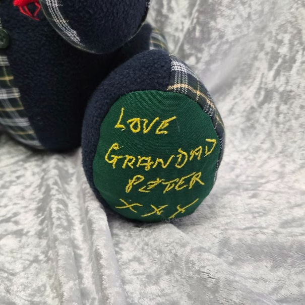 Memory bear made from navy and tartan clothing, featuring yellow stitched handwriting that reads “Love Grandad Peter xxx.