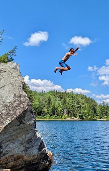 A boy jumpin from a high rock into Little Rock Pond