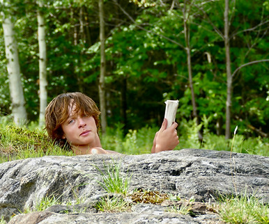 A boy lying on a rock outcrop while reading a book