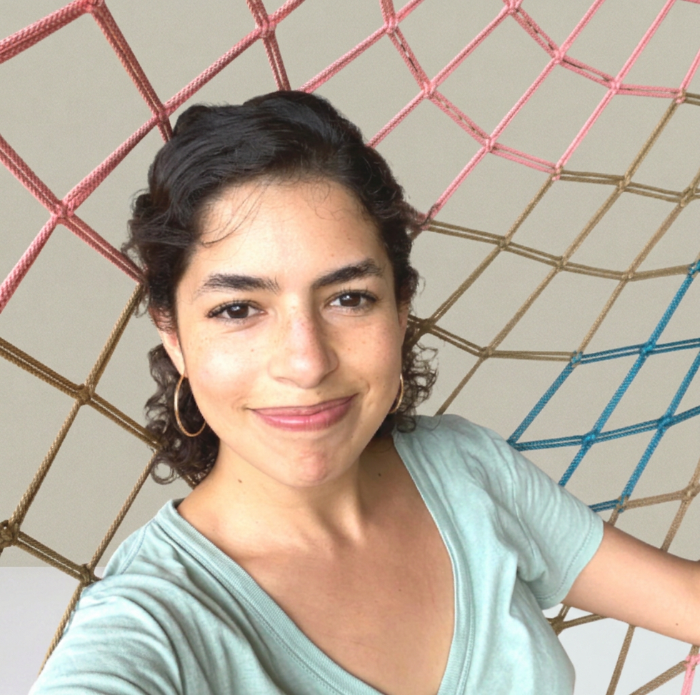 Portrait photography of a smiling young woman with dark curly hair. She is sitting in front of a colorful woven rope hammock, creating a relaxed and cheerful atmosphere.