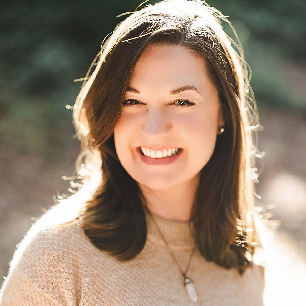 Smiling woman with brown hair in a beige sweater, wearing a necklace.