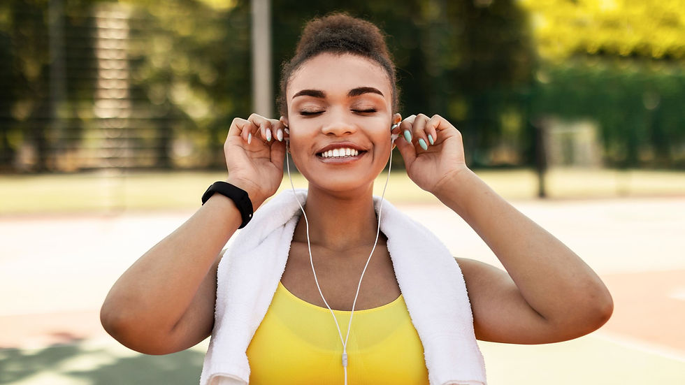 Smiling woman in a yellow sports top with towel and earbuds outdoors, adjusting her headphones after a workout