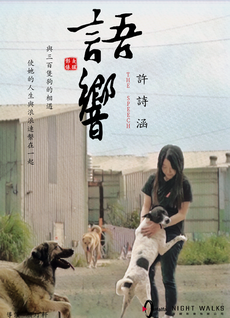 語響《親善動物-許詩涵》：一位黑衣女生，溫柔地摸著黑白相間的狗狗，狗狗鋪在女生身上，感受被照顧，旁邊還有一支黃黑色的大狗躺在地上。The speech film "Friendly Animals - Xu Shihan": A girl in black gently touches a black and white dog. The dog lies on the girl's body, feeling cared for. There is a big yellow and black dog lying on the ground next to her.