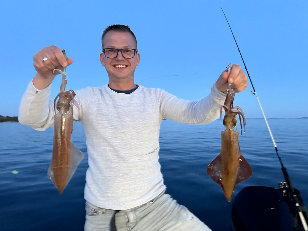 Smiling man holding two freshly caught Adriatic squids on a calm sea at sunset, with fishing rod in background.