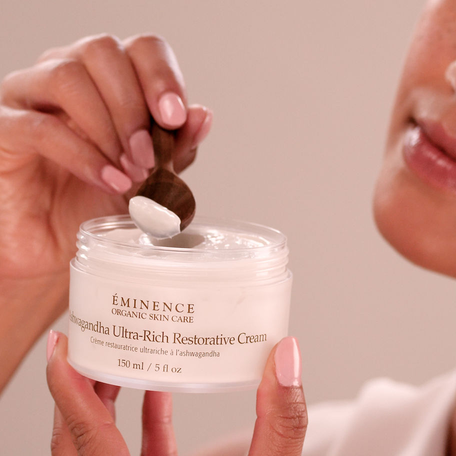 Woman scooping Eminence Ultra-Rich Restorative Cream with a wooden spoon, skin care.