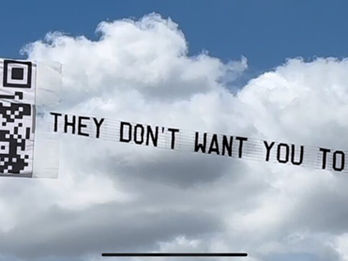Aerial billboard with trailing banner featuring a large QR code with a question mark icon and the message "THEY DON'T WANT YOU TO KNOW...." flying against a backdrop of white fluffy clouds, created in collaboration with The Skywriters, showcasing precision aerial advertising and high-impact event marketing.