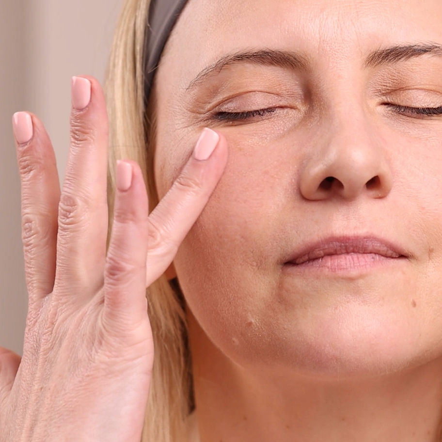 Woman gently touches her closed eye with fingers, applying skincare product.