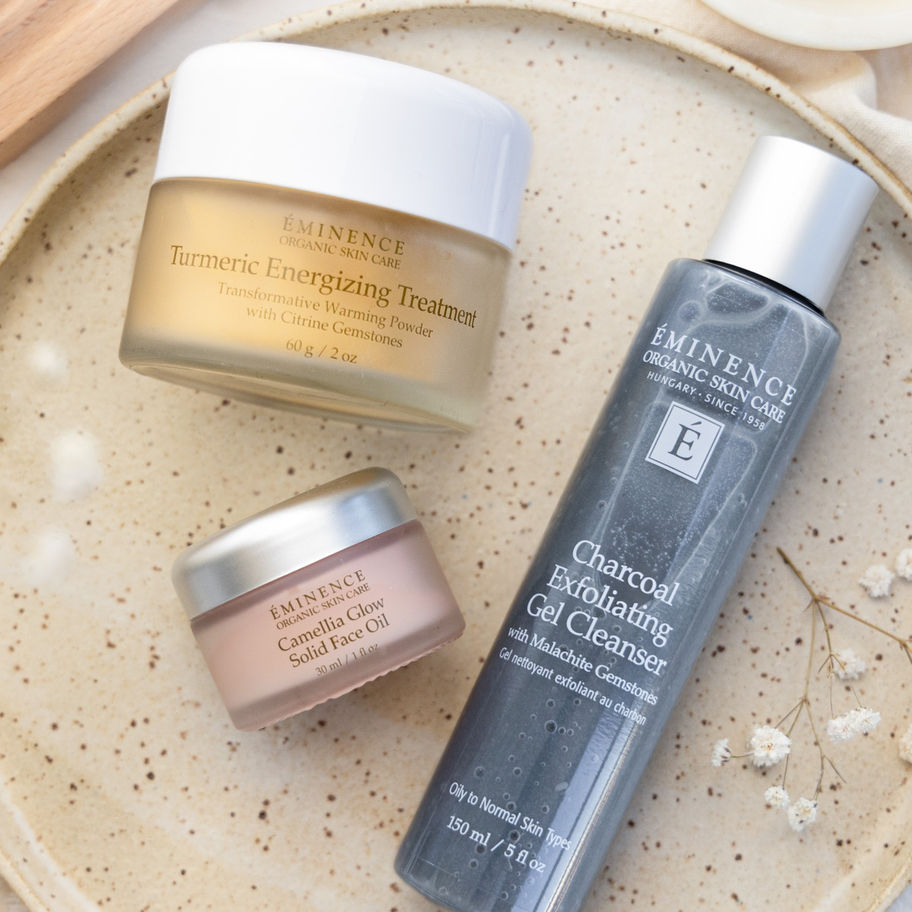 Three Eminence Organics skincare products on a ceramic plate; Charcoal, Cleanser.