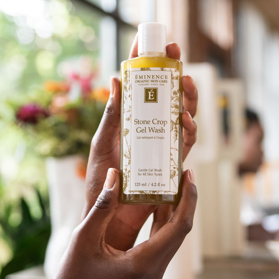 Person holding Rose Clay Gel Wash bottle with text, flowers in background.