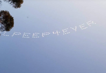 Professional skytyping spelling out LILPEEP 4 EVER in dot-matrix smoke letters visible past tree silhouettes against a clear blue sky, created in collaboration with The Skywriters, showcasing high-altitude skytyping services, broad-reach memorial messages, and moving aerial tributes.
