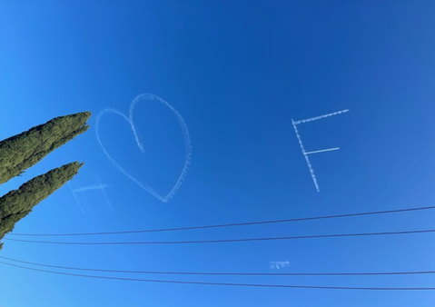 Marriage proposal event for a couple, while an airplane skywriting I Heart You message flies in the distance against a bright blue sky, created in collaboration with The Skywriters, showcasing professional aerial banner advertising, unique marriage proposal ideas, and high-impact aerial messaging for romantic celebrations.
