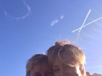 SIX skywriting message in flowing cloud letters above Ellen DeGeneres and Portia de Rossi in a sunny blue sky, created in collaboration with The Skywriters, showcasing precision skytyping, skywriting, aerial advertising, viral messaging opportunities, and creative wide area thoughtful gestures. 