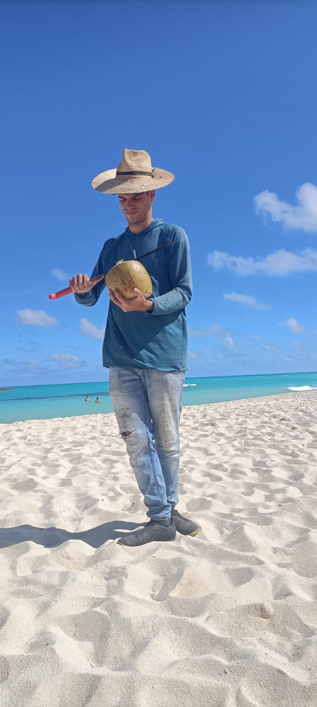 Uomo sulla spiaggia tiene cocco, cielo blu e mare turchese, My Site 1