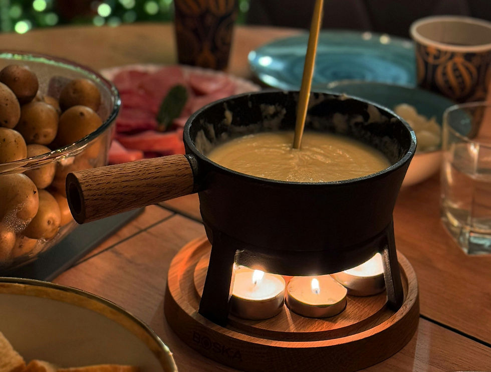 Cheese fondue pot with a wooden handle on a wooden table, surrounded by potatoes and meat slices. Warm lighting, cozy setting.
