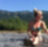 Dani Ross in a bikini sitting in the river with mountains in the background