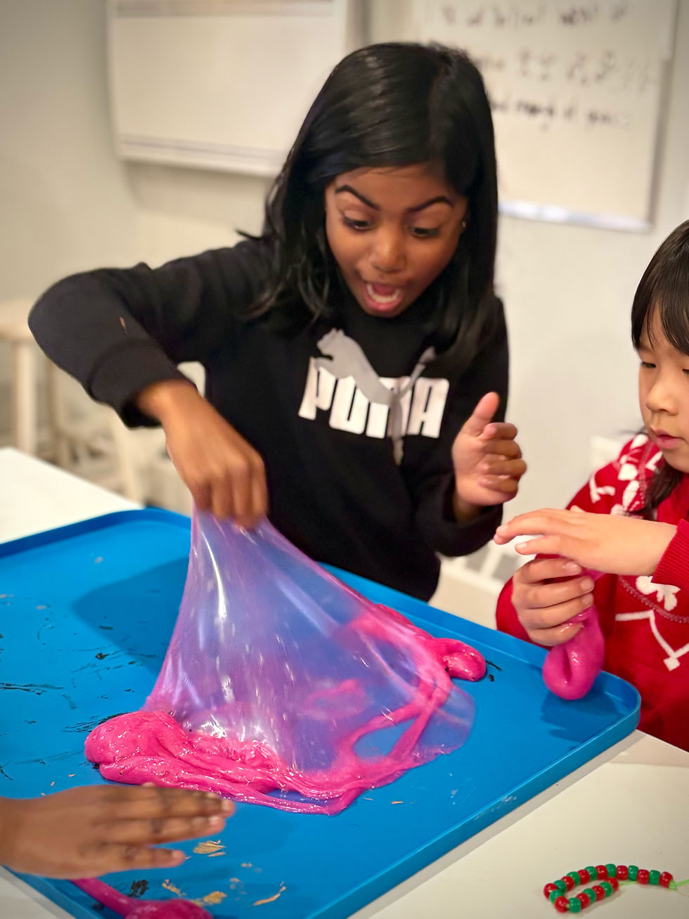 Two young students are experimenting with pink slime in the Makerspace classroom setting.