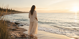 Woman standing barefoot in the water at the edge of the ocean watching the sun set.