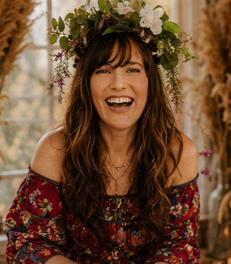 Tonya wearing a crown of flowers, laughing in front of a window.